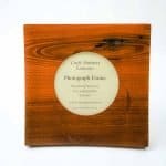 Round Photo picture jarrah frame (3) A handcrafted wooden photograph frame made from rich reddish-brown Jarrah hardwood. The square frame features a circular opening in the center displaying a printed label that reads: “Craft Partners Kalamunda – Photograph Frame – Handcrafted from Euc marginata ‘Jarrah’ – A West Australian hardwood.” The wood grain is beautifully visible, with natural variations and darker streaks that highlight the organic texture and craftsmanship of the piece.