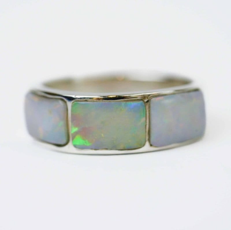Close-up of a sterling silver ring featuring three rectangular solid opal inlays. Each opal displays a luminous play of colour with flashes of green, blue, and red across a soft white base, highlighting the ring’s polished silver setting against a plain white background.