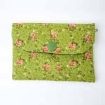 A handmade fabric coin purse with a flap closure secured by a green snap button. The purse features a soft green background patterned with small pink rosebuds and delicate vines, creating a vintage floral look. The fabric has a slightly textured appearance, and a small metal loop is visible on one side, possibly for attaching a strap or keychain. The purse is photographed flat against a plain white surface, highlighting its neat stitching and charming, cottage-style design.