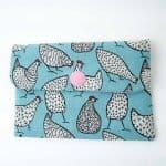 A handmade fabric coin purse with a flap closure secured by a pink snap button. The purse features a light blue background decorated with playful black-and-white chicken illustrations, each with unique geometric patterns such as stripes, dots, and crosses. The chickens have small red combs and thin black legs, creating a whimsical and fun design. The purse is photographed flat against a plain white surface, highlighting its cheerful and quirky pattern.