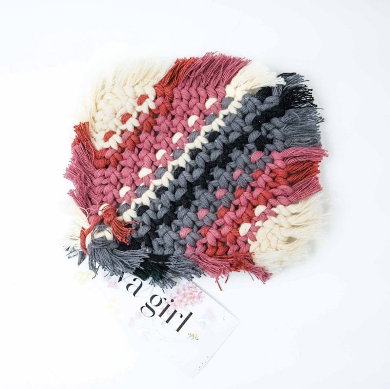 A square macramé drink coaster featuring alternating rows of rose, charcoal, and ivory cotton cord with fringed edges. The coaster is displayed on a white background with a WA Girl tag tucked underneath.