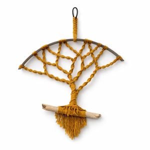 A handcrafted macramé wall hanging featuring a mustard‑coloured tree design knotted within a half‑circle metal frame, finished with a driftwood base and fringe, displayed against a clean white background.