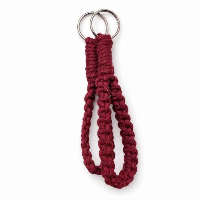 A handcrafted burgundy macramé wristlet keychain made from thick braided cotton cord, featuring two silver metal rings at the top. The wristlet is displayed against a clean white background with soft, even lighting and a subtle shadow beneath, highlighting its rich texture and deep colour.