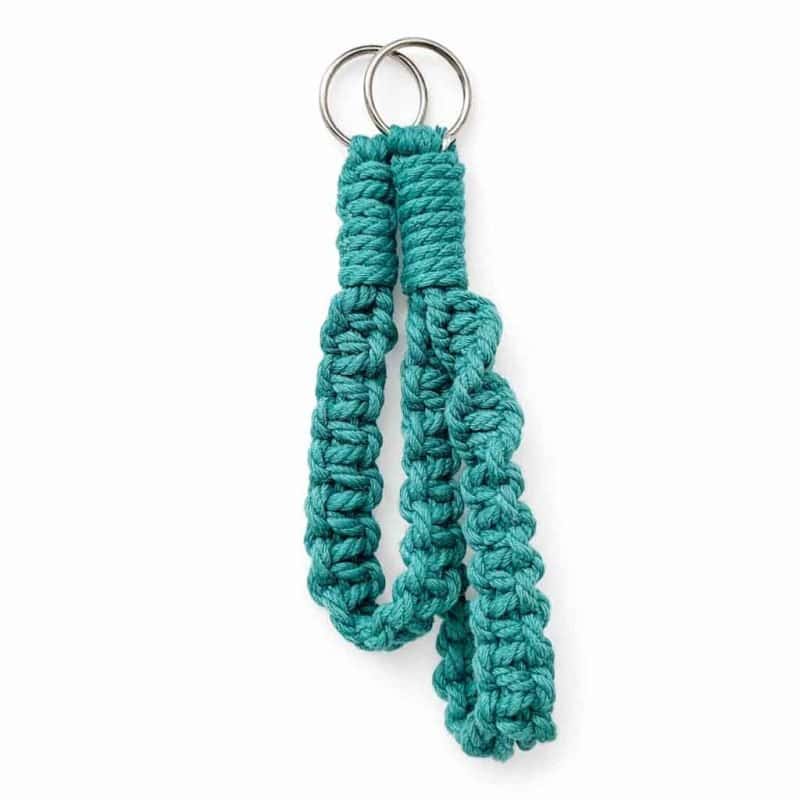 Two handcrafted teal macramé wristlets keychains made from thick braided cotton cord, featuring a silver metal ring at the top. The wristlets are displayed against a clean white background with soft, even lighting and a subtle shadow beneath, highlighting its texture and vibrant sea‑green colour.