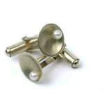 A close-up image of a pair of handcrafted sterling silver cufflinks displayed on a white background. Each cufflink features a concave circular face with a smooth satin finish and a single white freshwater pearl set near the center. The silver has a soft matte texture, and the cufflinks are arranged to show both the decorative face and the polished swivel bar mechanism. The composition highlights the elegant contrast between the lustrous pearl and the brushed silver surface.