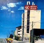 This striking original acrylic painting captures the gritty charm of urban life with bold color and confident brushwork. The Metro Hotel on the Highway to Hell depicts a towering city landmark under a vivid blue sky, its red signage glowing against the pale facade. Power lines, street poles, and graffiti lend the scene a raw, contemporary edge, while the composition’s clean geometry and saturated hues evoke a sense of rhythm and movement.