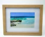 a painting of waves crashing on a beach with some rocks in an oak timber veneer frame. Signed by the artist Julie Eaton
