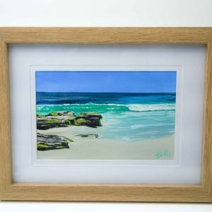 a painting of waves crashing on a beach with some rocks in an oak timber veneer frame. Signed by the artist Julie Eaton