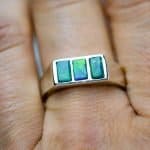 A close up of the opal ring. The ring is being worn on the finger of a light-skinned woman