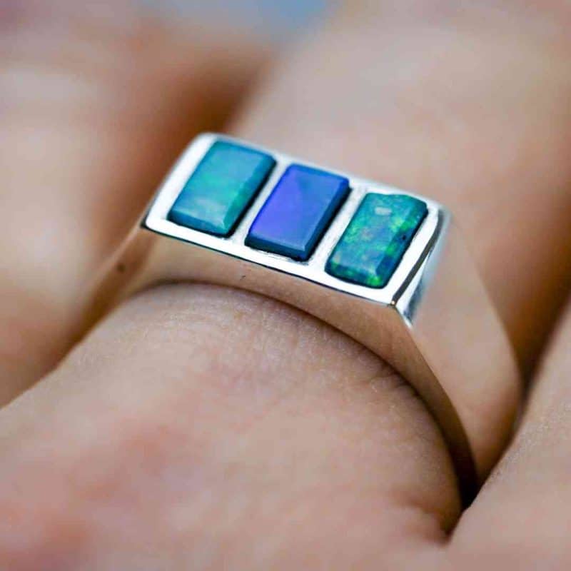 A sterling silver ring with 3 cetangular opals as a centre piece. Theopals are blue-green in colour.