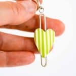 Corrugated Heart Earrings Green corrugated heart earrings are displayed on a white background. Each earring features a vertically striped enamel heart suspended within a slender sterling silver frame. One pair has bright lime green and white stripes with gold hoops, while the other pair has blue and white stripes with silver hoops. The design is modern and playful, showcasing handcrafted detail and vibrant colour contrast.