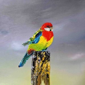 An oil painting of an Eastern Rosella perched on a weathered wooden post. The bird’s plumage is vividly rendered with thick, textured strokes of red, yellow, green, and blue, standing out against a softly blended grey and pale yellow background. The artist’s signature, Sue Adams, appears in the lower right corner, adding a refined finishing touch to the composition.