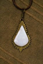 Freeform Opal Pendant (1) The teardrop-shaped opal pendant lays flat on a wooden background.