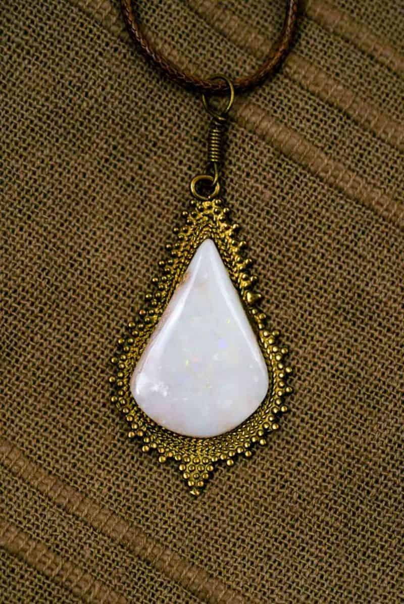 The teardrop-shaped opal pendant lays flat on a wooden background.