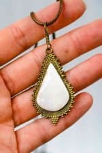 Freeform Opal Pendant (4) A teardrop- shaped pendant made from a large opal set into an antique-style golden setting. The pendant is being held in an open palm.
