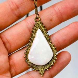 A teardrop- shaped pendant made from a large opal set into an antique-style golden setting. The pendant is being held in an open palm.