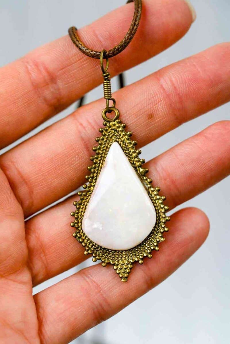 Freeform Opal Pendant (4) A teardrop- shaped pendant made from a large opal set into an antique-style golden setting. The pendant is being held in an open palm.