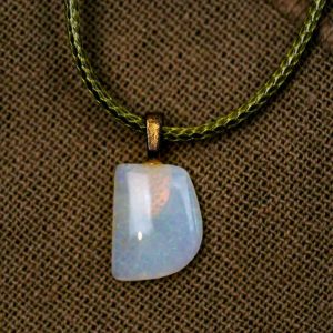 A rectangular opal pendant hangs from a green wax-necklace. The opal lays on a brown background