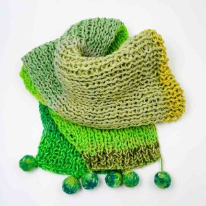 A knitted scarf folded on a white background. The scarf is made from different tones of green and has 6 felted pom poms hanging from the ends