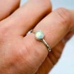 Green+Yellow opal in sterling Silver (1) A delicate opal shining with yellows and greens is set on a thin sterling silver band. The ring is being worn on the pointer finger of a fair-skinned woman.