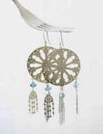 A pait of silver earrings suspended from a metal fork. The earrings are similar to a cathedral window, with three hanging jellyfish below. Each jellyfish has a blue diamond-shaped bead above it