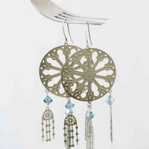 A pait of silver earrings suspended from a metal fork. The earrings are similar to a cathedral window, with three hanging jellyfish below. Each jellyfish has a blue diamond-shaped bead above it
