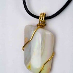 A large white opal pendant is wrapped in golden wire and attached to a black wax necklace. The open shimmers in shades of green, purple, and orange