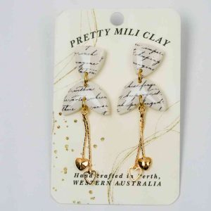 A dangley pair of earrings on a display piece of card. The earrings are made from a piece of paper with illegible cursive writing sealed in polymer clay in a triangle shape, followed by an upside down love heart. Beneath the polymer clay pieces is a gold chain with small hearts on the end.