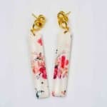 Pink flower drop earrings (2) The floral polymer clay earrings lay flat on an off-white background. The earrings sit slightly askew due to the fastening