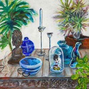 Still‑life painting featuring a wooden table arranged with blue glass vessels, a small sculpted head, tall candle holders, and a glass dome containing a figurine of a woman in a yellow patterned dress. The table is surrounded by lush green and purple‑tinted plants, creating a rich, decorative composition