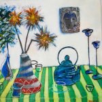 Colourful still‑life painting featuring a green and yellow striped tablecloth with blue teapots, cups and vases arranged on top. One vase holds bright orange and yellow spiky flowers, while another contains blue foliage. A decorative wall piece with a stylised face and ornate patterns appears in the background, adding a bold, expressive focal point