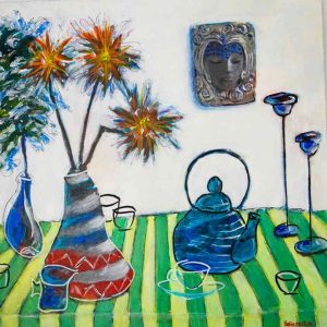 Colourful still‑life painting featuring a green and yellow striped tablecloth with blue teapots, cups and vases arranged on top. One vase holds bright orange and yellow spiky flowers, while another contains blue foliage. A decorative wall piece with a stylised face and ornate patterns appears in the background, adding a bold, expressive focal point