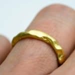Close-up of a handcrafted solid 18ct gold ring worn on a finger. The ring features a gently irregular, organic texture with a soft matte sheen, highlighting its artisanal design and natural form.