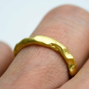 Close-up of a handcrafted solid 18ct gold ring worn on a finger. The ring features a gently irregular, organic texture with a soft matte sheen, highlighting its artisanal design and natural form.