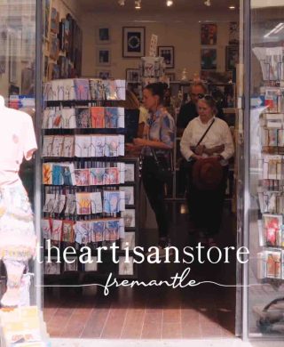 Entrance to The Artisan Store Fremantle, showing customers browsing racks of colourful art prints and framed artworks inside a bright, welcoming retail space that showcases locally made pieces.