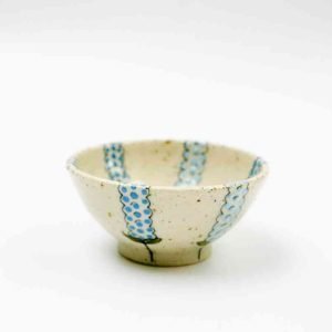 Handcrafted ceramic bowl with a speckled cream glaze and vertical blue dotted stripes evenly spaced around its exterior and interior. The bowl has a slightly flared rim and a small footed base, photographed against a clean white background to highlight its texture and painted detail.