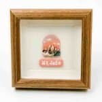 Winimum Handmade -Mt Jade framed A small framed artwork featuring a depiction of Mt. Jade, with rugged peaks under a warm pink and orange sky. Below the illustration, a matching pink plaque displays the words “Mt. Jade” in white lettering. The piece is set within a wooden frame against a white background, creating a clean and elegant presentation.