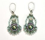 A pair of handcrafted beaded earrings featuring an intricate teardrop design. Each earring has a shimmering iridescent centre bead surrounded by small glass beads in shades of sage green, lilac, and pearl. The earrings are finished with silver lever-back hooks and arranged against a plain white background, highlighting their detailed texture and elegant craftsmanship.