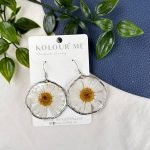 A Pair of circular earrings made from a pressed white daisy flower, captured in resin with silver frames.