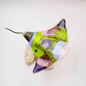 A top-down image of a colourful eagle ray made of glass. It is made from a combination of glass textures and colours, showcasing an array of greens, purples, pink, and with gold accents painted atop the coloured glass.