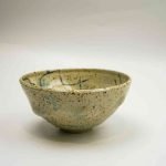 A sand-coloured ceramic bowl spattered with different tones of blue sits against a white background