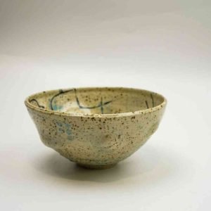 A sand-coloured ceramic bowl spattered with different tones of blue sits against a white background