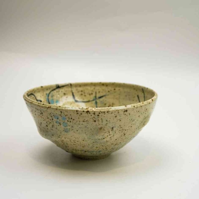 A sand-coloured ceramic bowl spattered with different tones of blue sits against a white background