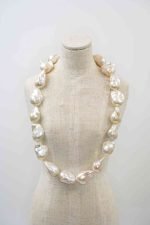 Jumbo Pearl Strand Colleen Brennan (4) A beige linen mannequin displaying a necklace made of large, irregularly shaped white baroque pearls. Each pearl has a lustrous, organic surface with soft iridescent tones of cream and silver. The necklace drapes naturally around the mannequin’s neck, highlighting the unique size and texture of each pearl against the neutral background.