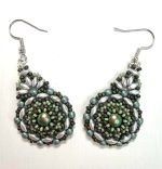 A pair of handcrafted beaded earrings with a teardrop shape, featuring a shimmering iridescent green centre surrounded by intricate layers of small glass beads in shades of sage, silver, and dark olive. The earrings are finished with silver hooks and displayed against a plain white background, highlighting their detailed texture and elegant artisan design.
