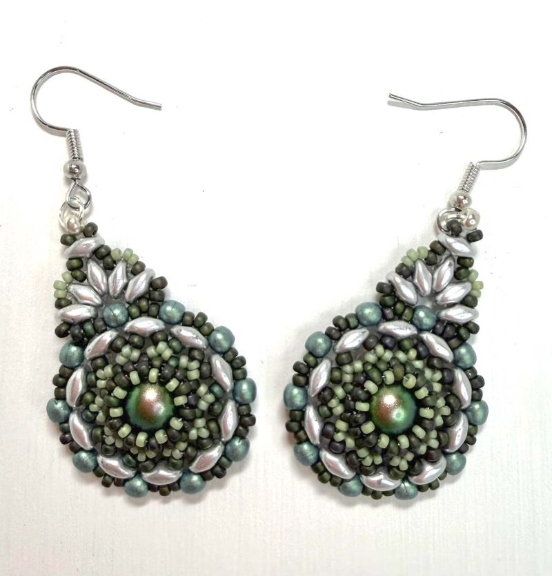 A pair of handcrafted beaded earrings with a teardrop shape, featuring a shimmering iridescent green centre surrounded by intricate layers of small glass beads in shades of sage, silver, and dark olive. The earrings are finished with silver hooks and displayed against a plain white background, highlighting their detailed texture and elegant artisan design.