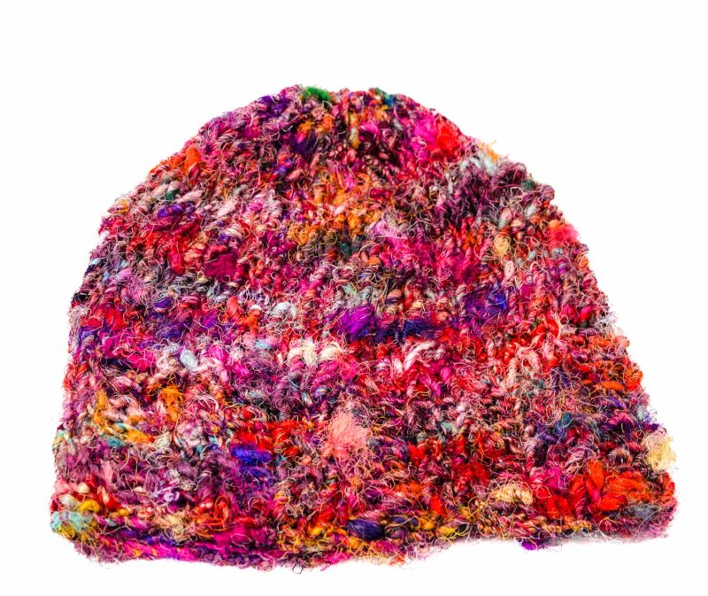 Knitted silk yarn red multicolour beanie (2) An image of a multicoloured, red-based, knitted beanie laying on a white surface