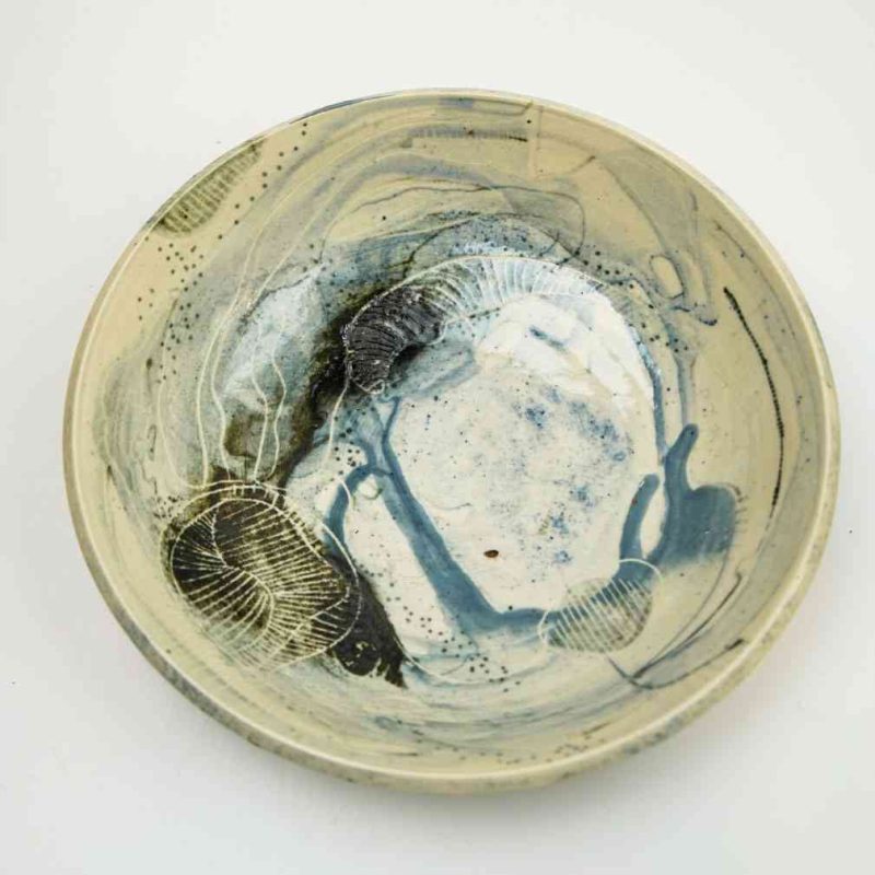 A large cermaic bowl decorated with abstract blue glaze. The bowl is viewed from the top down showing the interior of the bowl, and sits on a white background