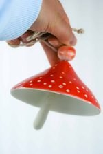 A second image of the mushroom wind chime, this time a fair-skinned person in a blue long sleeve holds the mushroom, displaying it's underside and size.