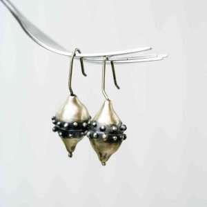 Two conical shaped earrings hang from a silver fork. Their middle is made of oxidized silver and decorated with small silver granules